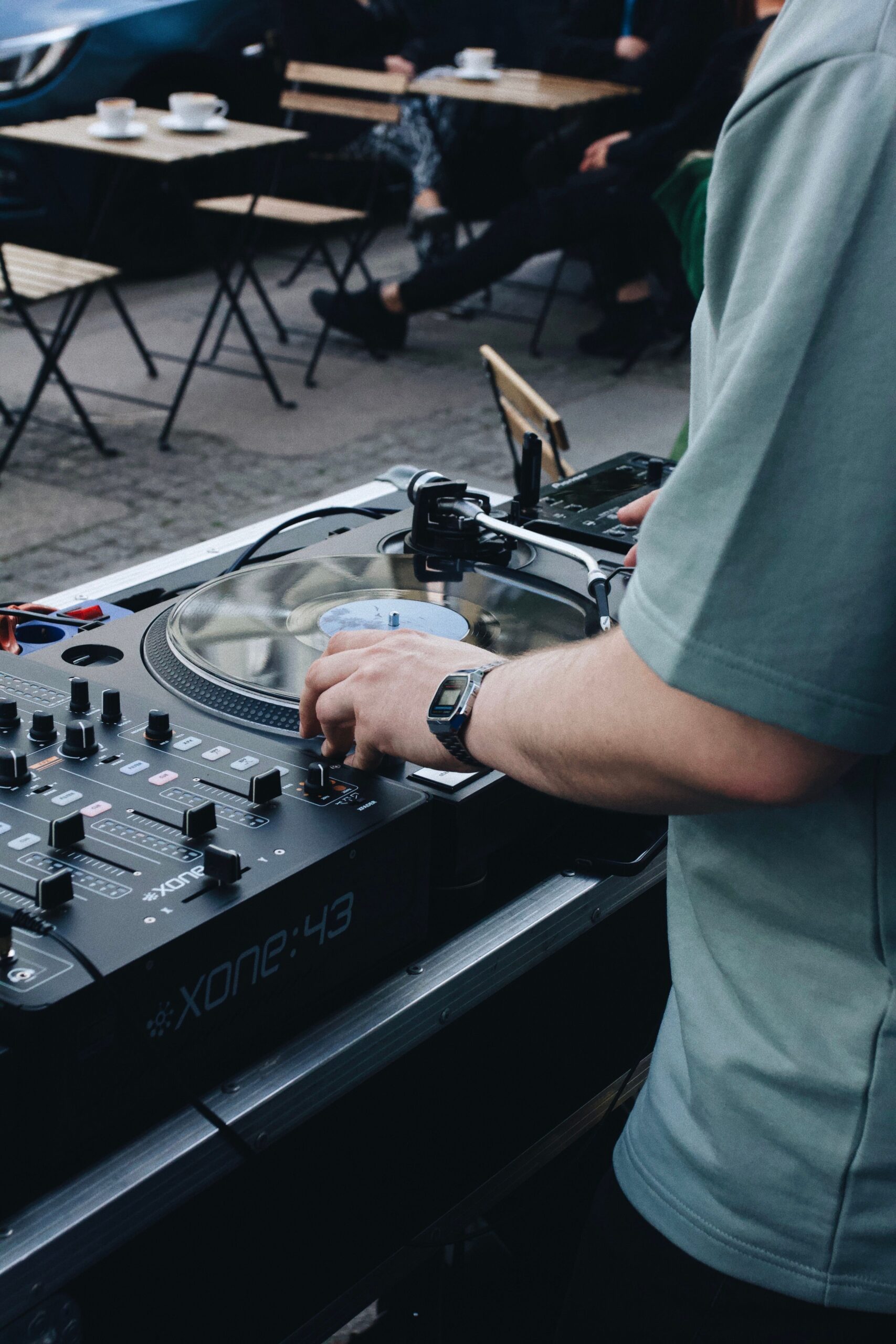 Best corporate and wedding DJ near me adjusting audio mixer at an outdoor café in Alabama creating vibrant tunes.